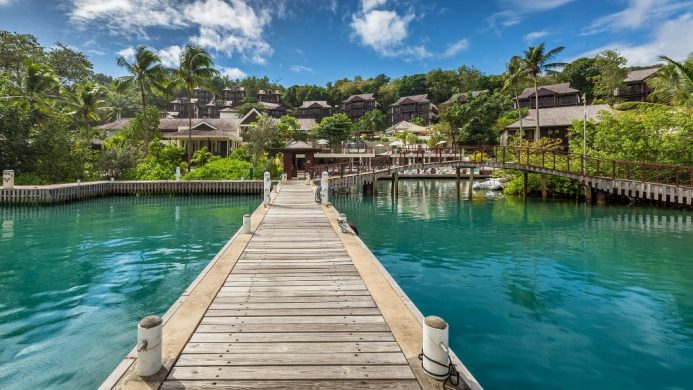 Overwater walkway leading to resort amidst palm tree forest