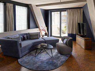 Modern living room with blue couch, coffee table, TV and closed balcony with curtains