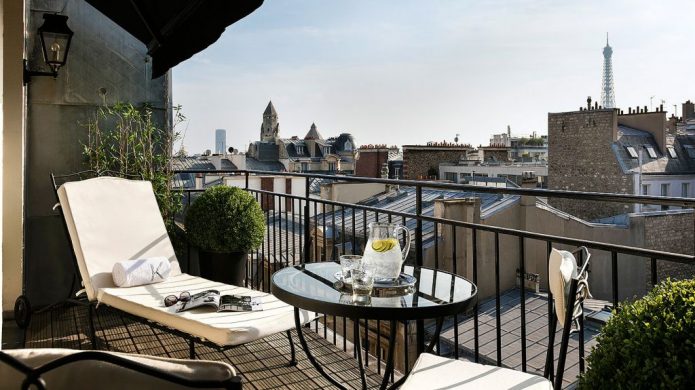 Balcony with patio chair and lounge chairs with view of rooftops and Eiffel Tower