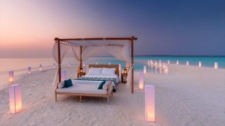 Four poster bed on isolated sandback with lanterns