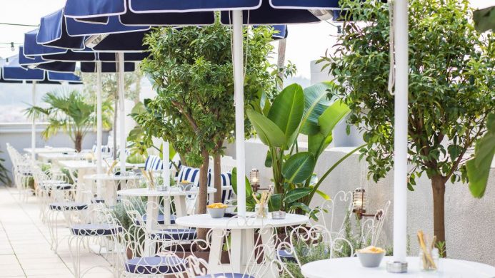 Outdoor terrace with white patio bistro tables and chairs surrounded by potted greenery