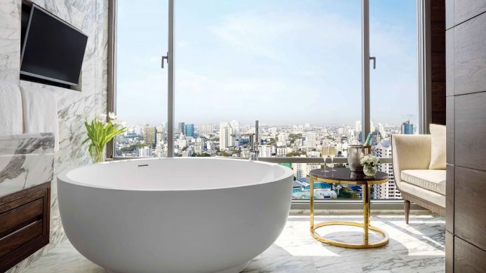 Round bathtub in marble bathroom with floor-to-ceiling window view of Bangkok