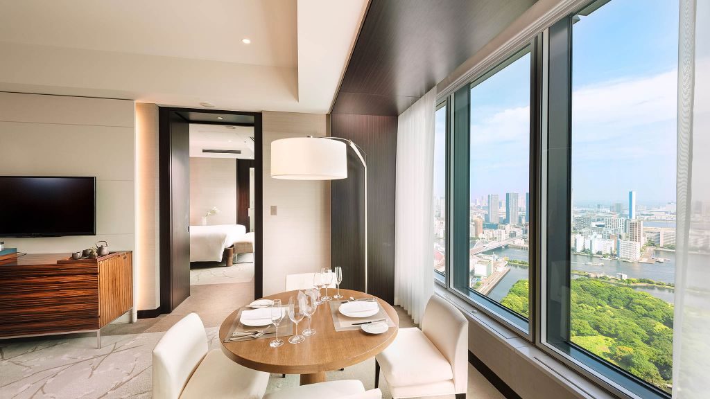 Suite with dining area and windows overlooking Tokyo and green gardens