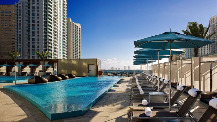 Rooftop pool with lounge chairs and umbrellas, surrounded by tall buildings