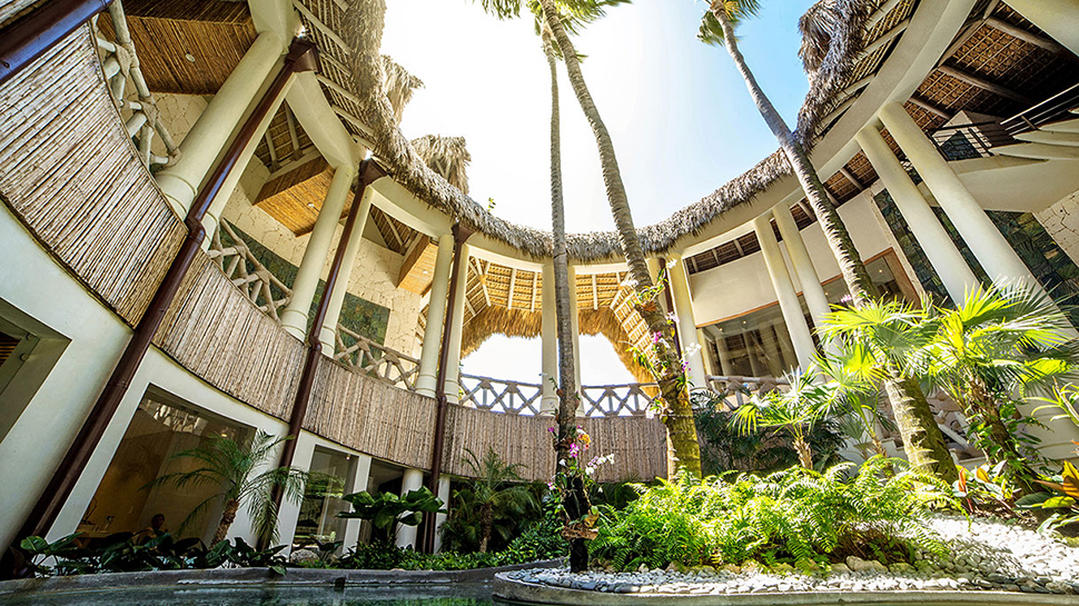 Eden Roc Wellness spa courtyard with water, palm trees and thatched roof