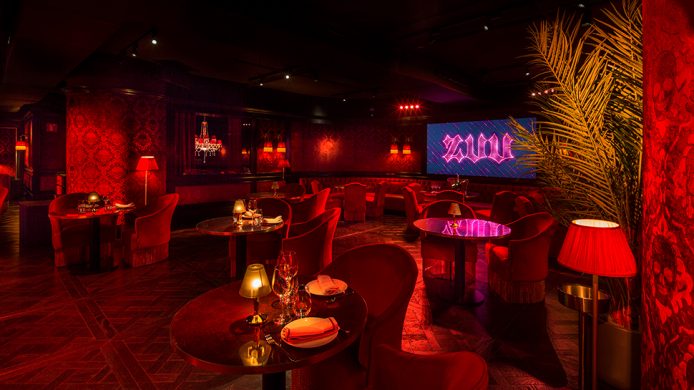 Dark restaurant and stage with red velvets at Hotel SOFIA Barcelona's Zuu restaurant and cabaret