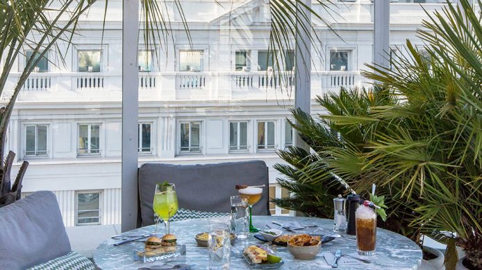 Outdoor table surrounded by green plants in a glass-enclosed terrace