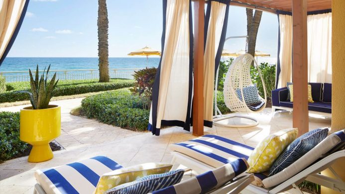 Oceanfront lanai with nautical curtains and loungers and a swing chair at the Eau Palm Beach Resort and Spa