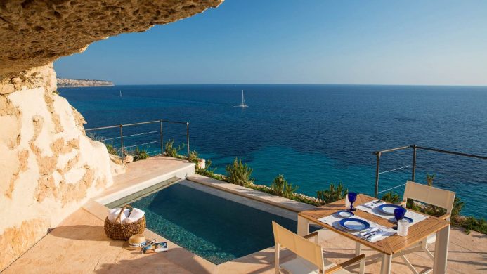 Plunge pool overlooking blue waters and sailboat under within sandstone