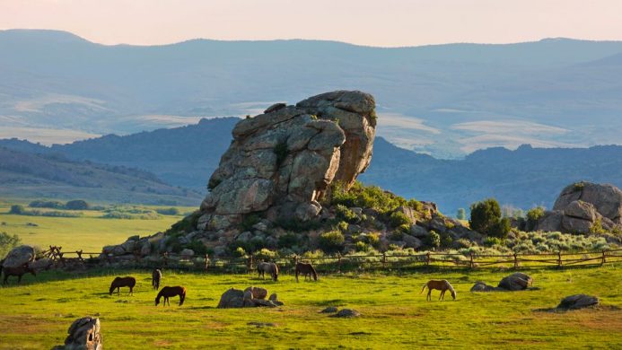 Horses grazing in front of rock formation at The Brush Creek Ranch