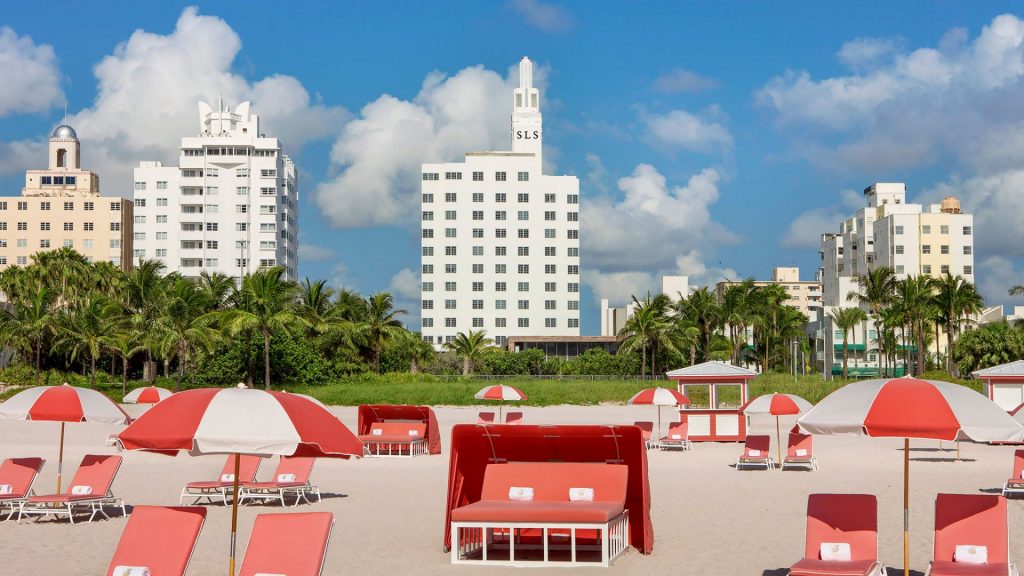 SLS South Beach hotel behind a beach with coral-colored chairs and umbrellas