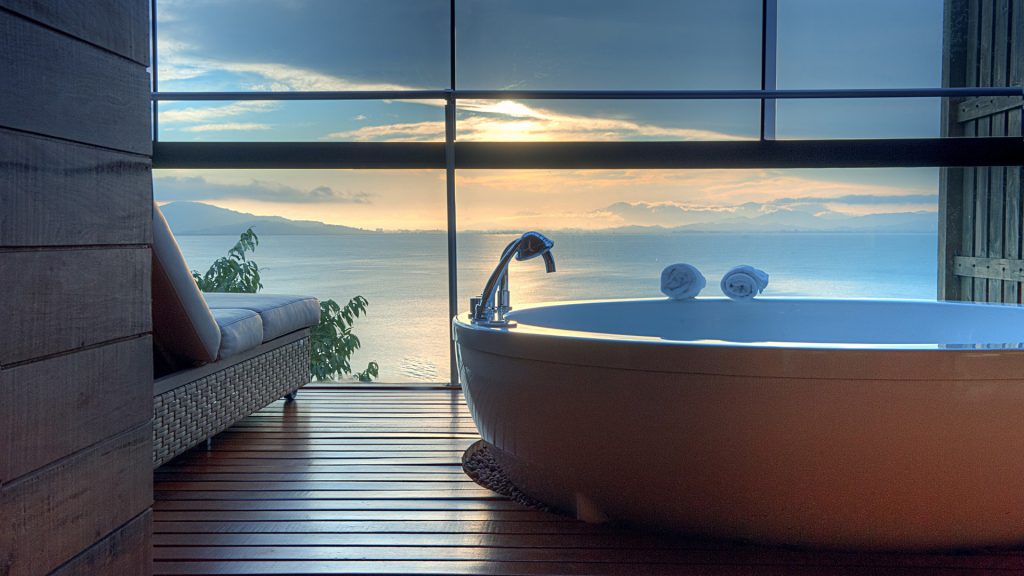 Oval bathtub inside the Esmeralda Bungalow at Ponta dos Ganchos Exclusive Resort, in front of a sun set view on the horizon