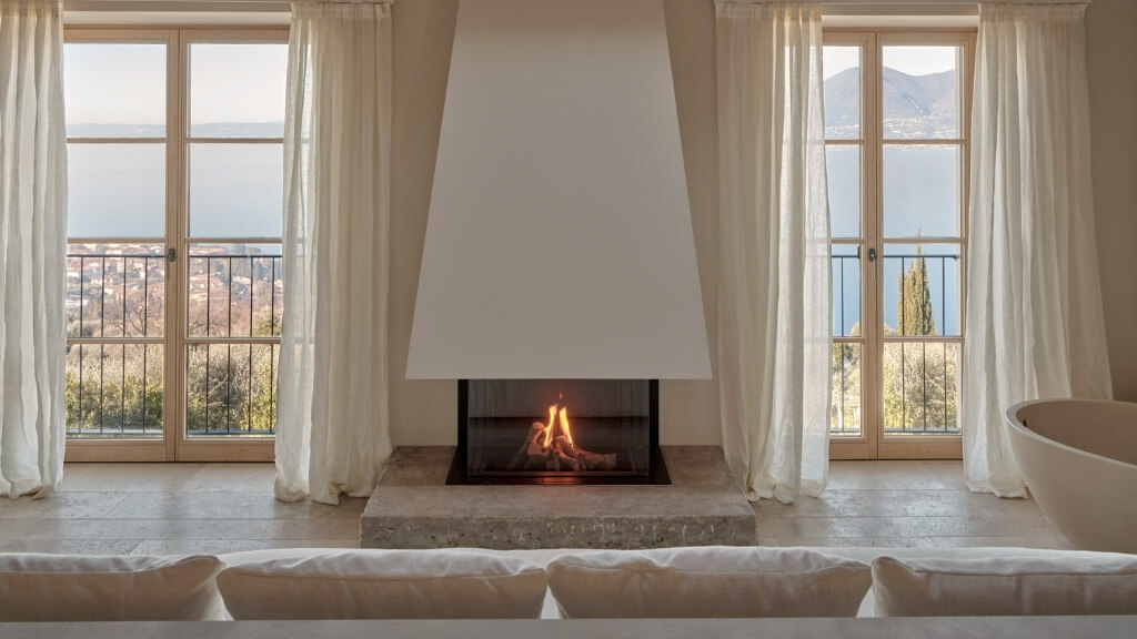 Small hotels | Borgo Tre Lake Garda, Lake Garda, Italy | a fireplace in a room with windows and a view of the mountains and Lake Garda