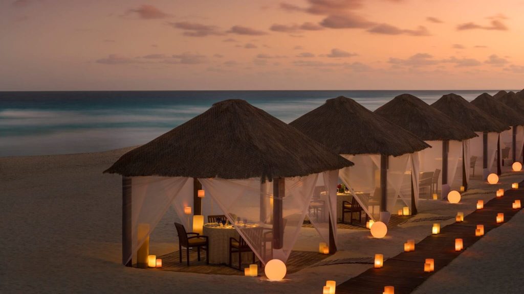 Sunset cocktails at Kempinski Hotel Cancún | Cancun, Mexico | a group of cabanas with candles on the beach at sunset