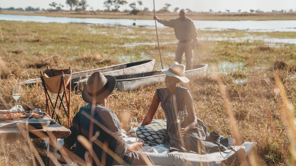 Picnic spots - Belmond Eagle Island Lodge - Okavango Delta, Botswana - two people on a picnic blanket and one person in the background in a boat