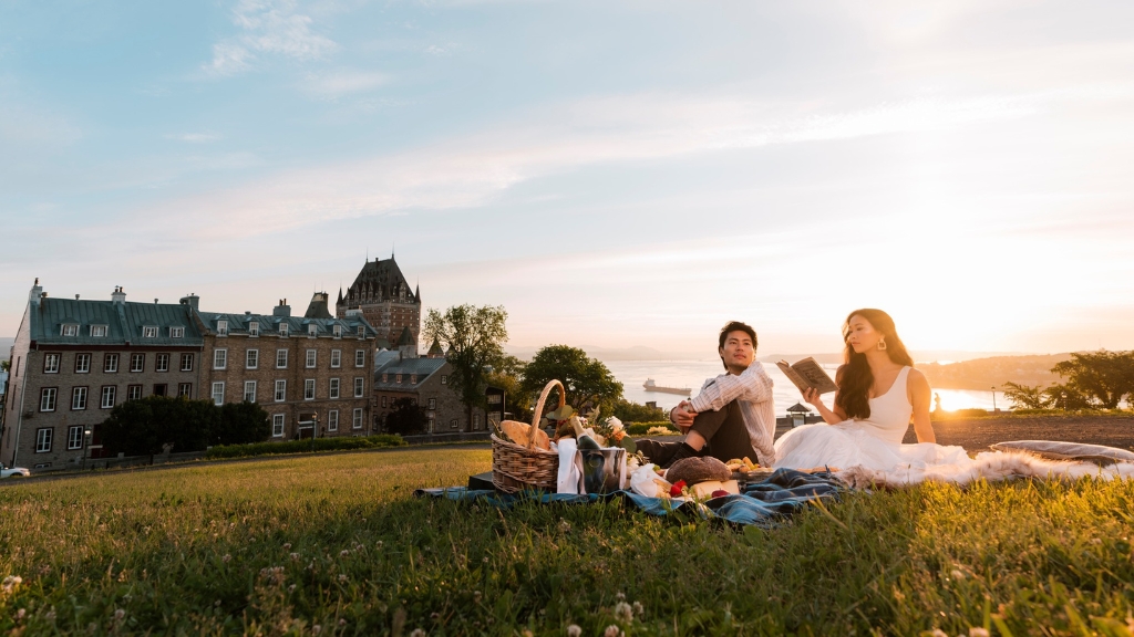 Picnic spots - Fairmont Le Château Frontenac - Québec City, Canada - two people sitting on a picnic blanket with the hotel and St. Lawrence River in the background