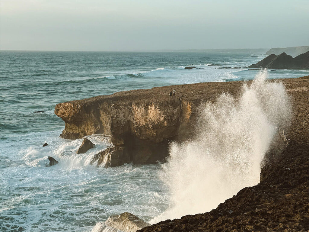 Portugal and Spain Travel Diary Itinerary by Christine Flynn - a large wave crashing on a rocky cliff in The Algarve, Portugal