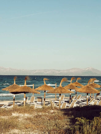 Portugal and Spain Travel Diary Itinerary by Christine Flynn | a beach with straw umbrellas and chairs at Sarena de Muro Resort Mallorica, Spain