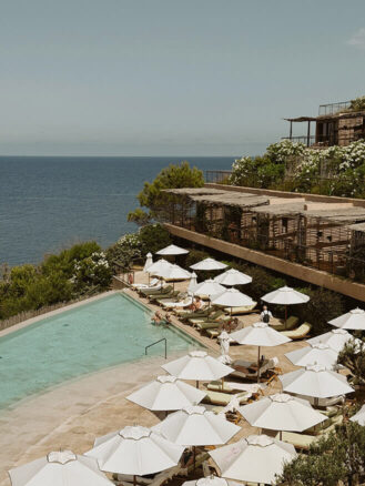 Portugal and Spain Travel Diary Itinerary by Christine Flynn | a pool with umbrellas and chairs and a building overlooking the sea at Six Senses Ibiza, Spain